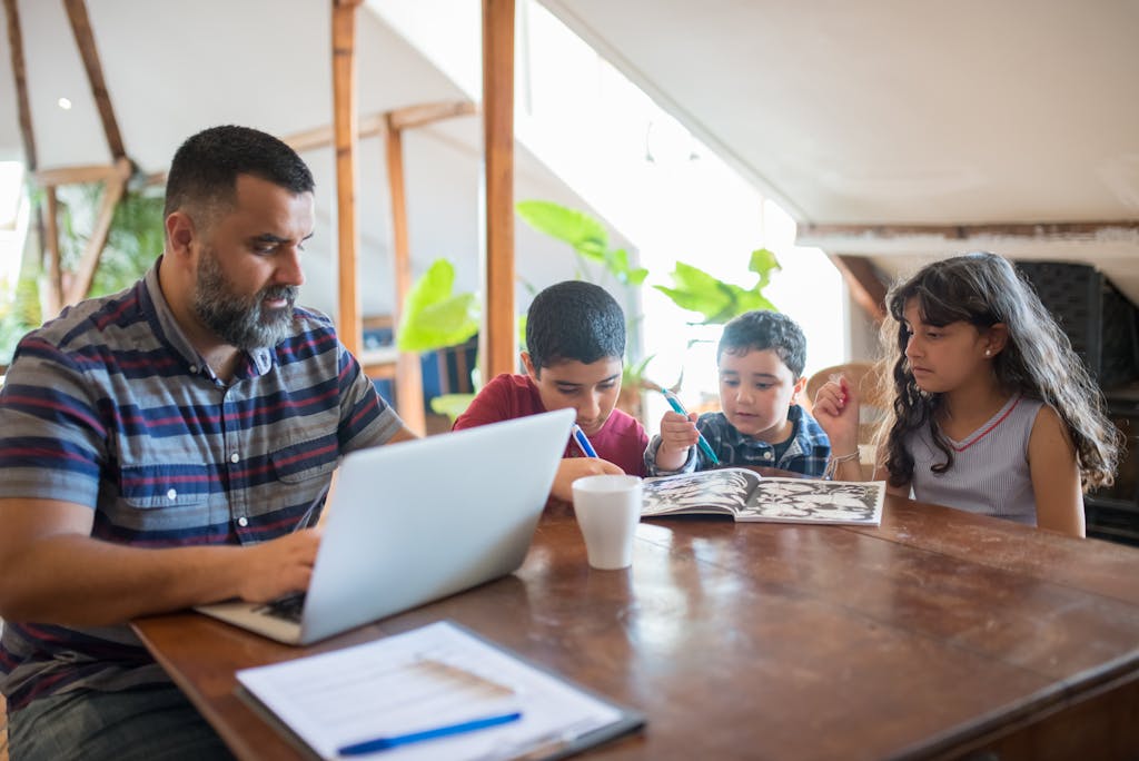 A father multitasks with a laptop and children at home, illustrating work-life balance.